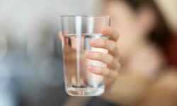 Eine Hand hält ein Glas mit klarem Wasser. Der Hintergrund ist unscharf, wodurch der Fokus auf dem Glas liegt.